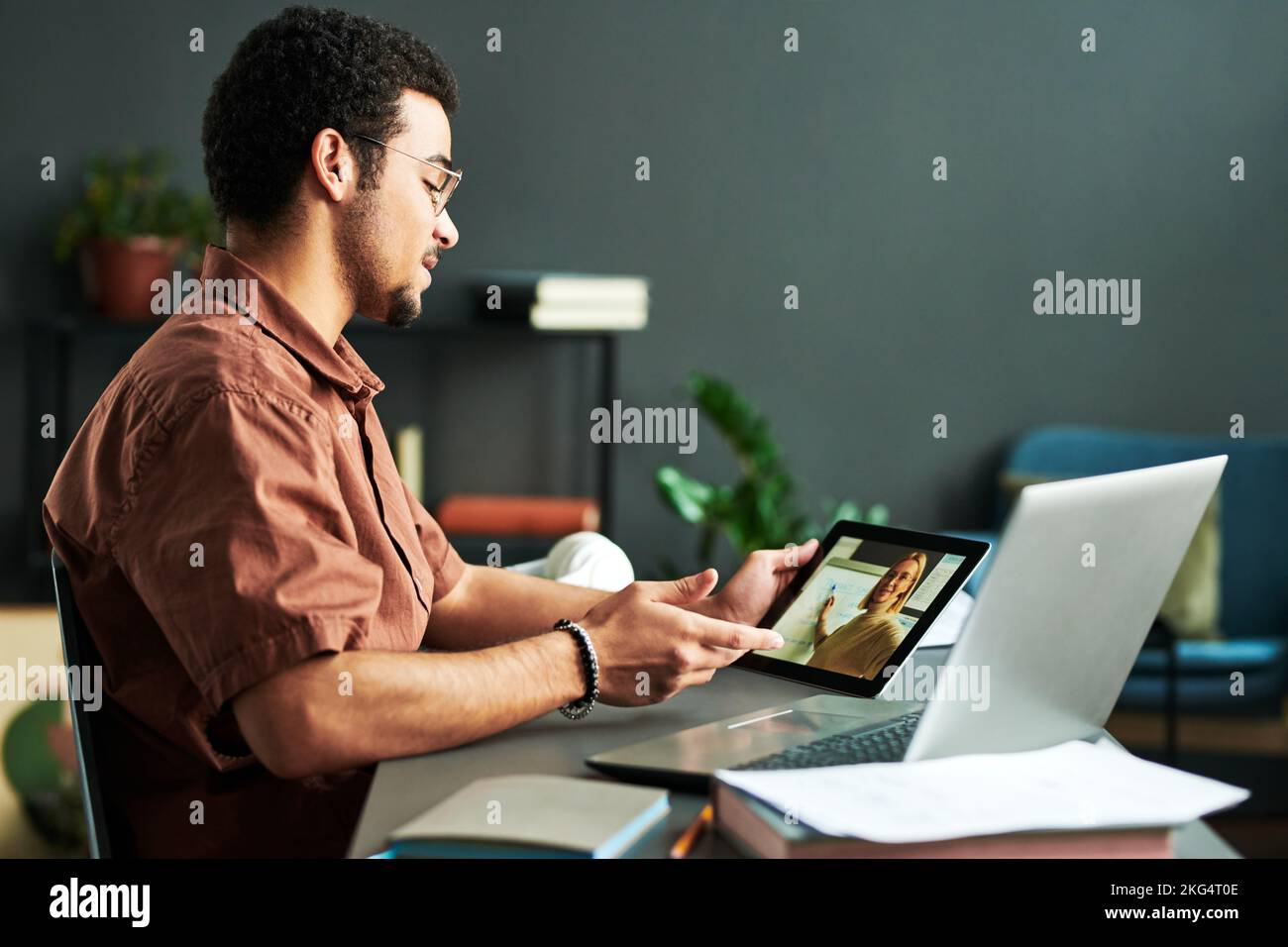 Junger selbstbewusster Mann, der den Lehrer ansieht, der während des Online-Unterrichts eine Präsentation auf dem Tablet-Bildschirm macht und Punkte zu neuen Themen diskutiert Stockfoto