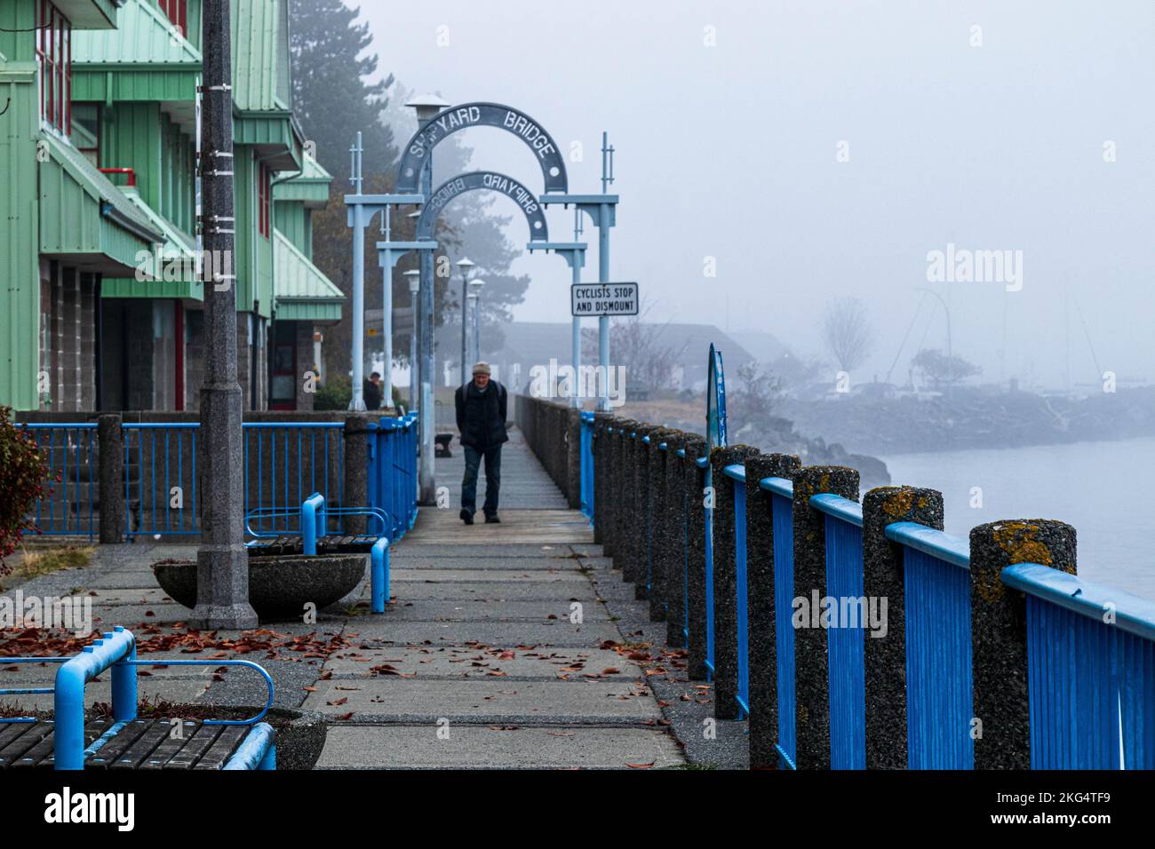 Der Fußweg am Wasser war im Nebel und ein alter Mann ging auf dem Holzweg. Friedliche, ruhige Szene mit altmodischen Straßenlaternen. Stockfoto