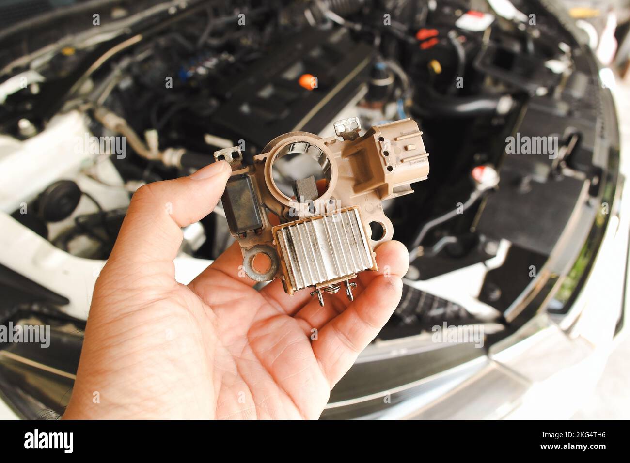 Alte Gleichrichter Automobil-Lichtmaschine halten von Auto-Mechaniker Hand mit Auto-Motorraum verschwommen Hintergrund Stockfoto