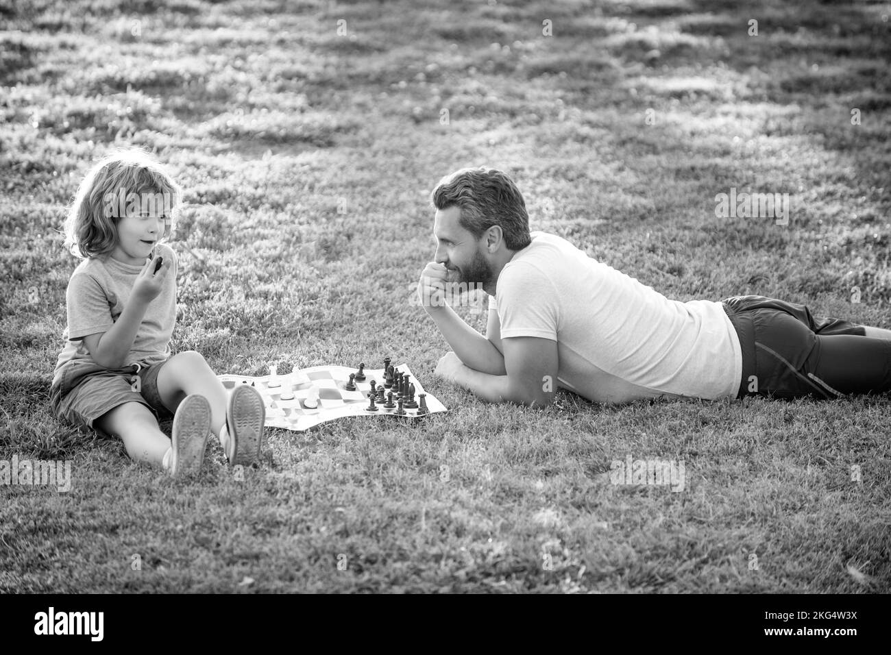 Vater und Sohn spielen Schach auf Gras im Park. Vatertag. Glückliche Familie. Elternschaft und Kindheit. Stockfoto