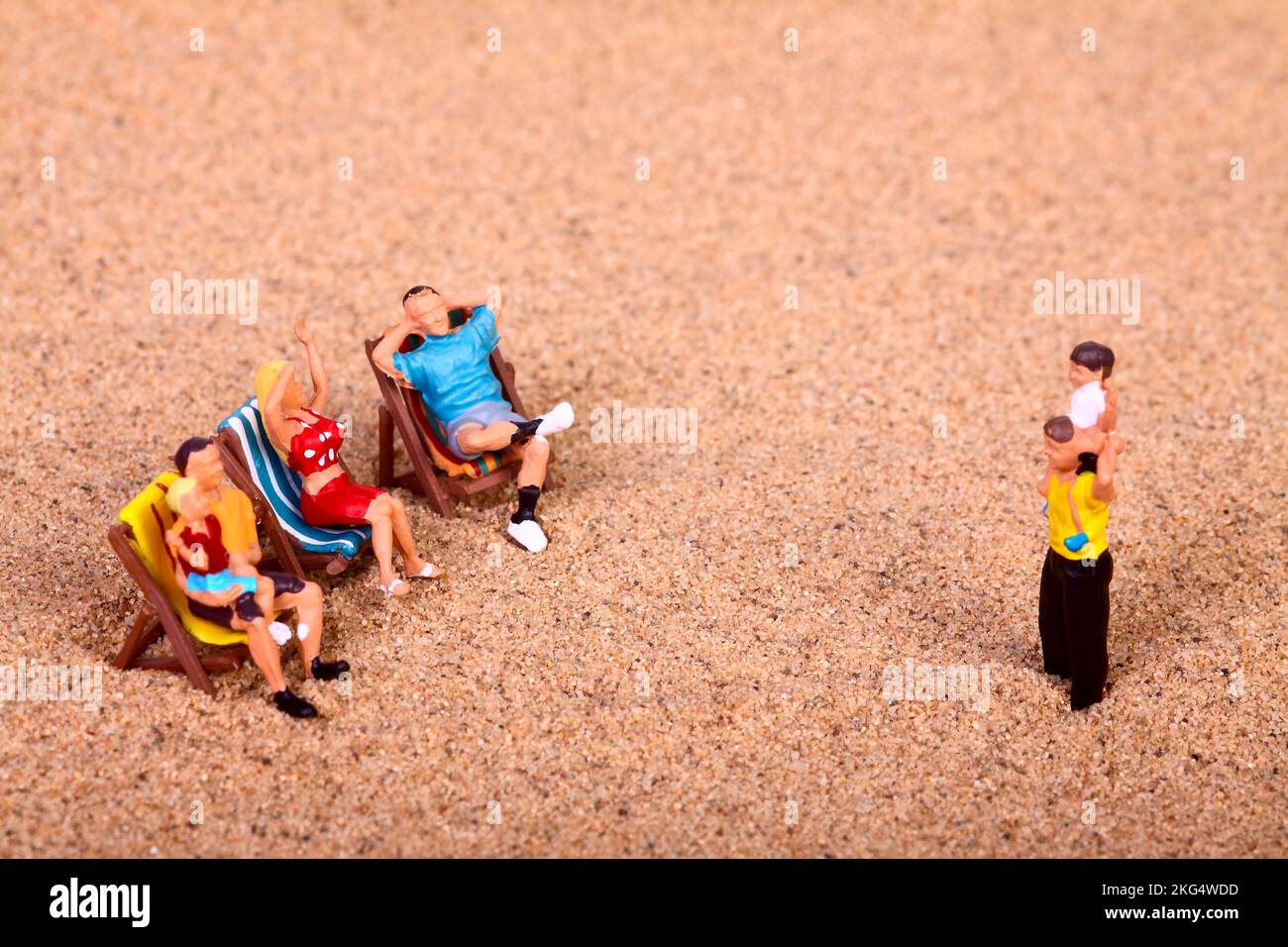 Konzeptionelles Bild einer Miniaturfigur, Leute saßen auf Liegestühlen an einem Sandstrand, Urlaubskonzept Stockfoto