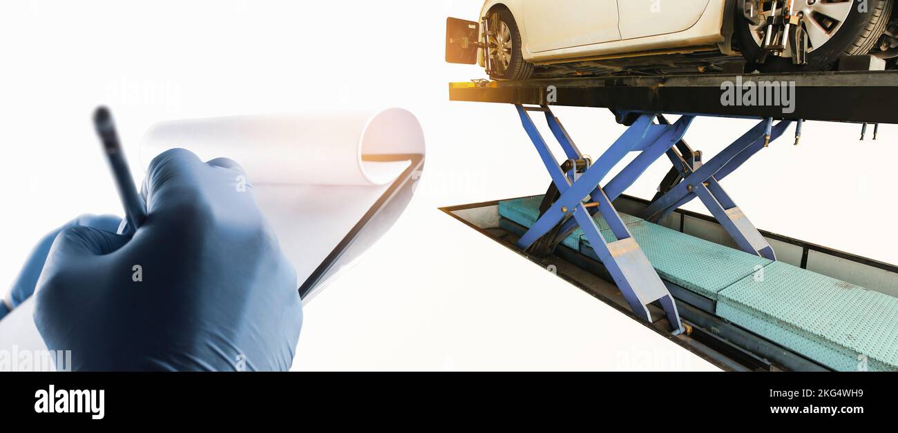 Der Mechaniker nimmt Notizen auf Papier für die Analyse der Auto-Probleme eines weißen Autos auf hydraulischen Autolift, Auto-Wartung Service-Konzept Stockfoto