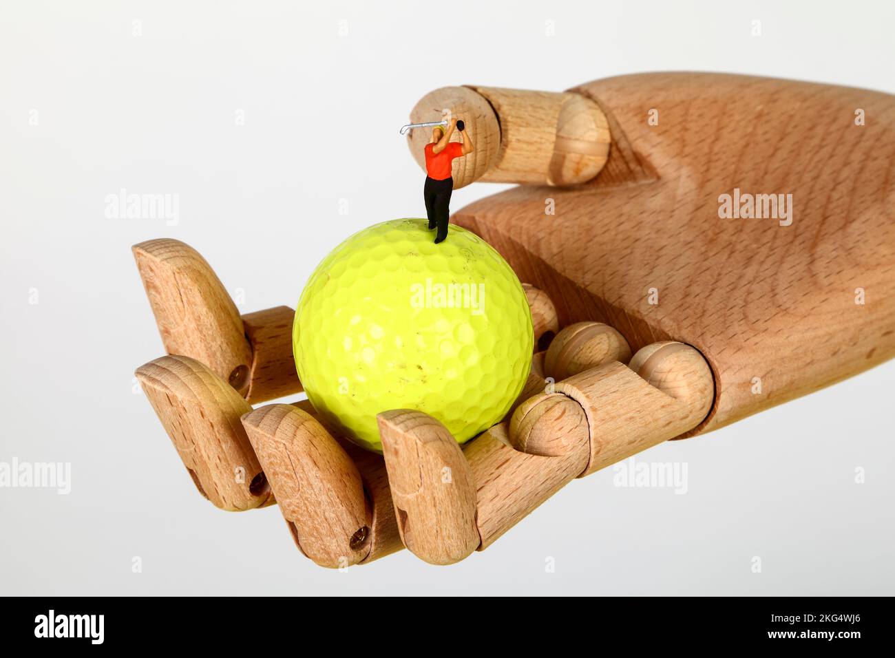 Konzeptionelles Bild einer Minigolferin, die sich von einem Golfball in einer hölzernen Hand abschlägt Stockfoto