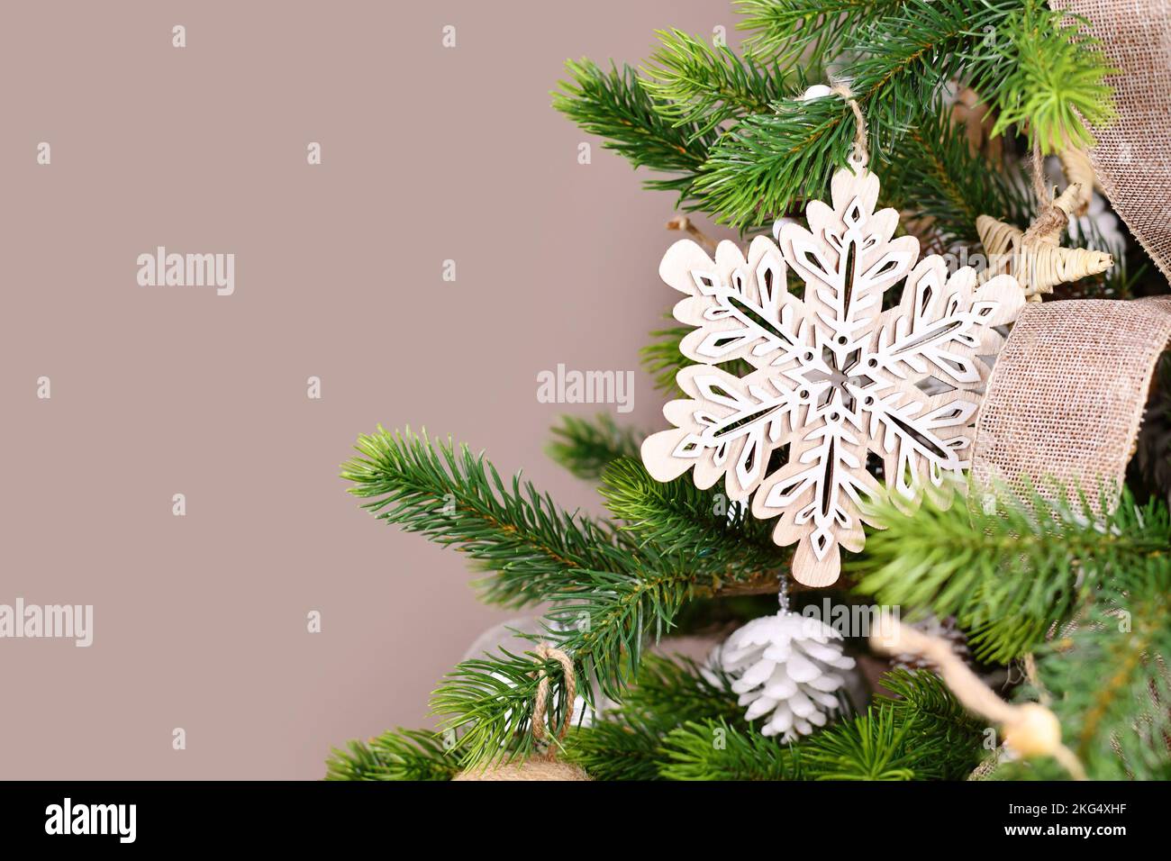 Weihnachtsbaumzweig mit natürlicher Holzschneeflocke vor beigefarbenem Hintergrund mit Kopierbereich Stockfoto