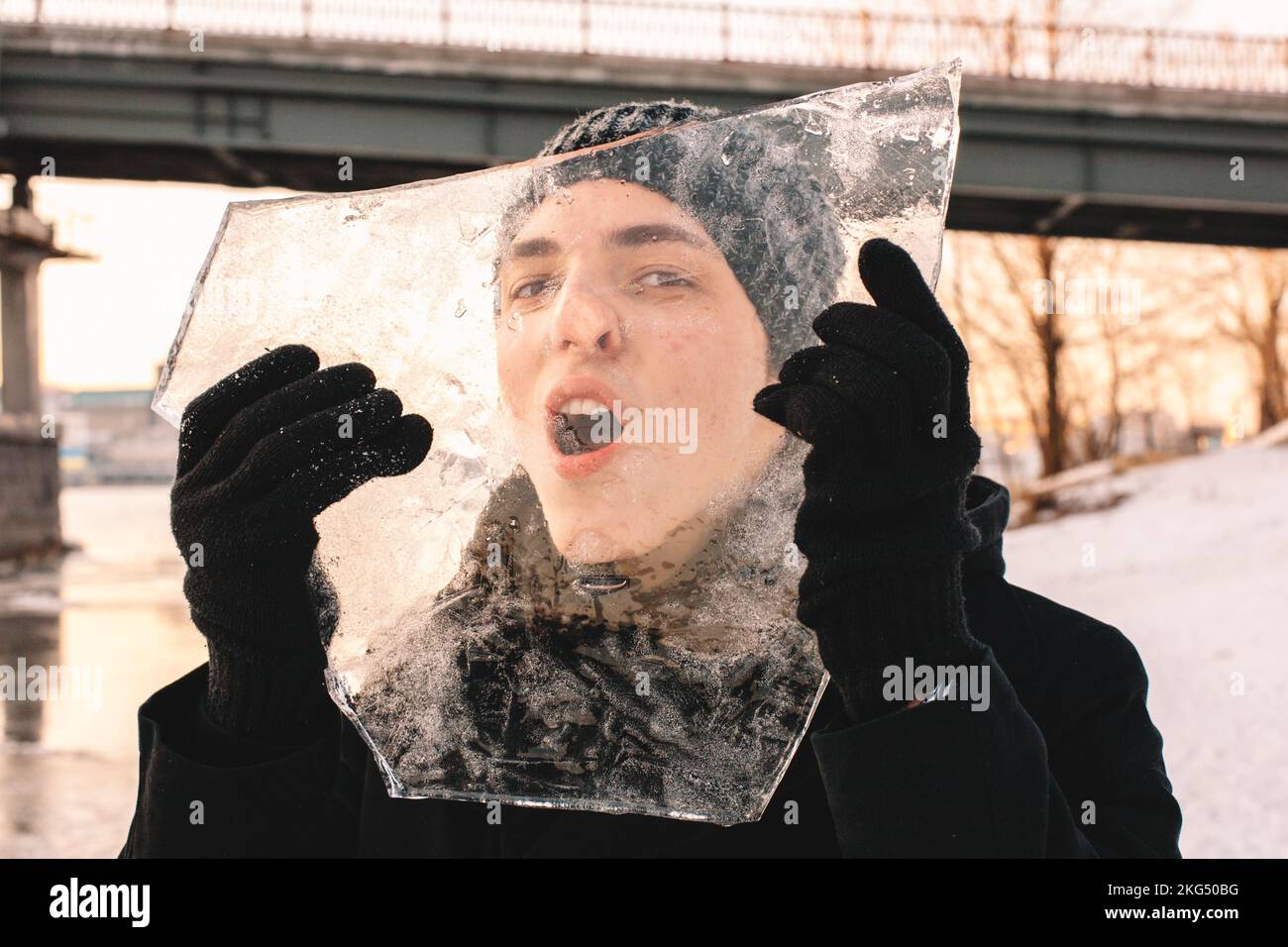 Teenager-Junge, der bei kaltem, frostigem Wetter im Winter durch ein Stück Eis schaut und es im Freien hält Stockfoto