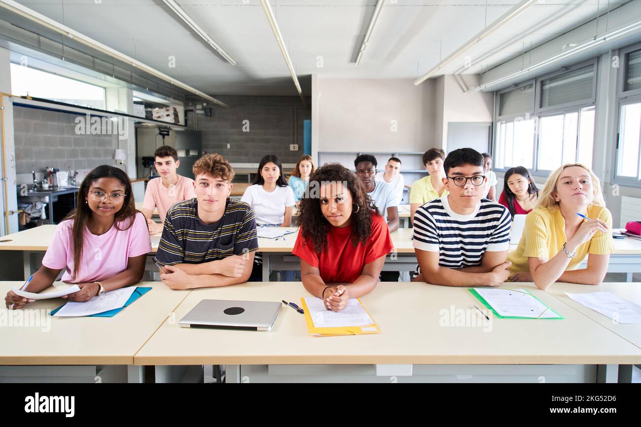 Eine selbstbewusste Gruppe von Universitätsabsolventen, die im Klassenzimmer sitzt und mit ernstem Gesicht in die Kamera schaut. Porträt von Schülern der Highschool zusammen Stockfoto