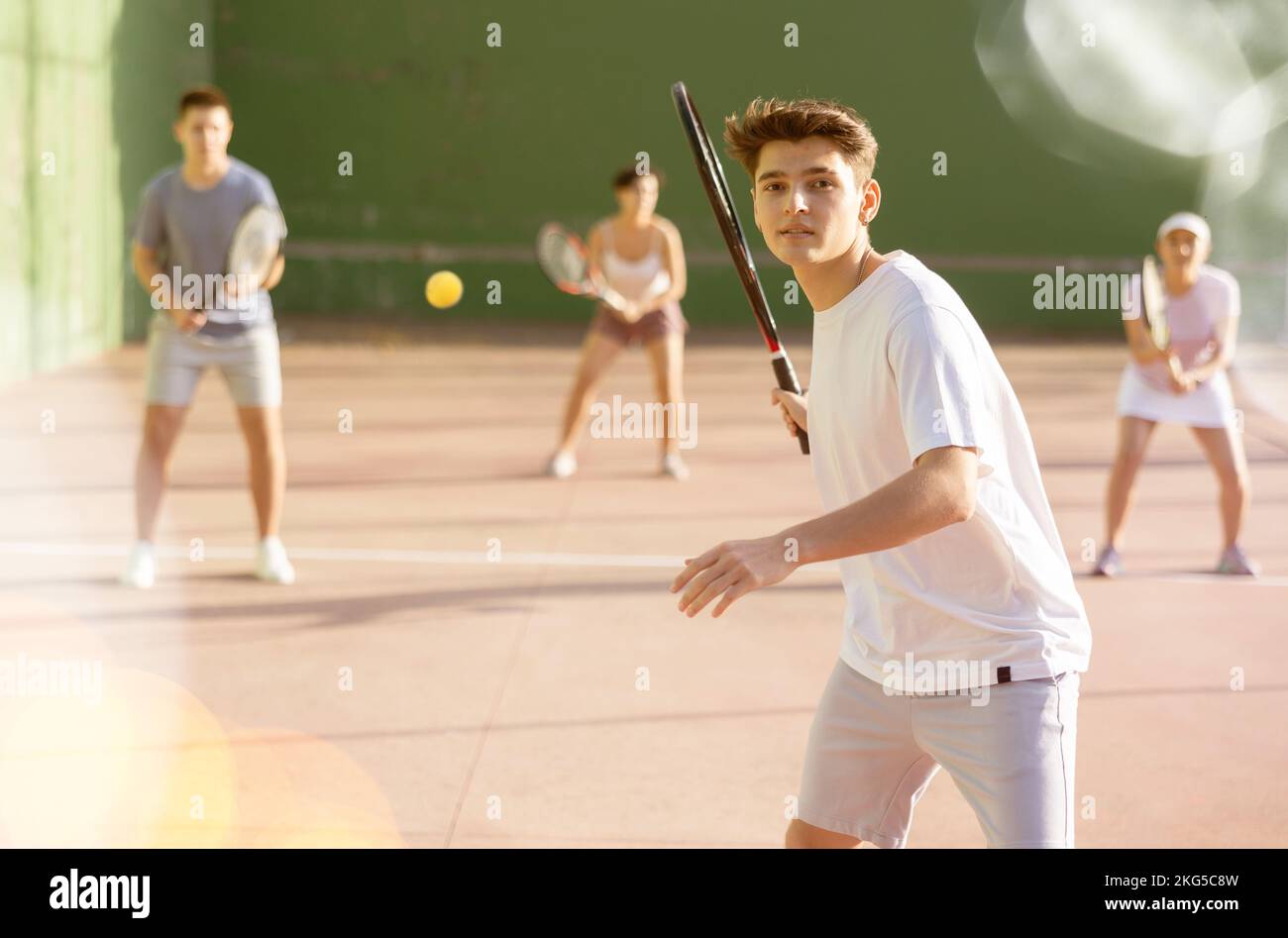 Guy trifft den Ball mit einem Schläger, während er Frontenis auf dem Platz im Freien spielt Stockfoto