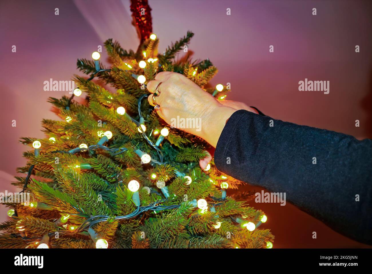 Frauenhände mit Ringen kittrige elektrische Lichter auf künstlichem Weihnachtsbaum - Nahaufnahme und selektiver Fokus Stockfoto