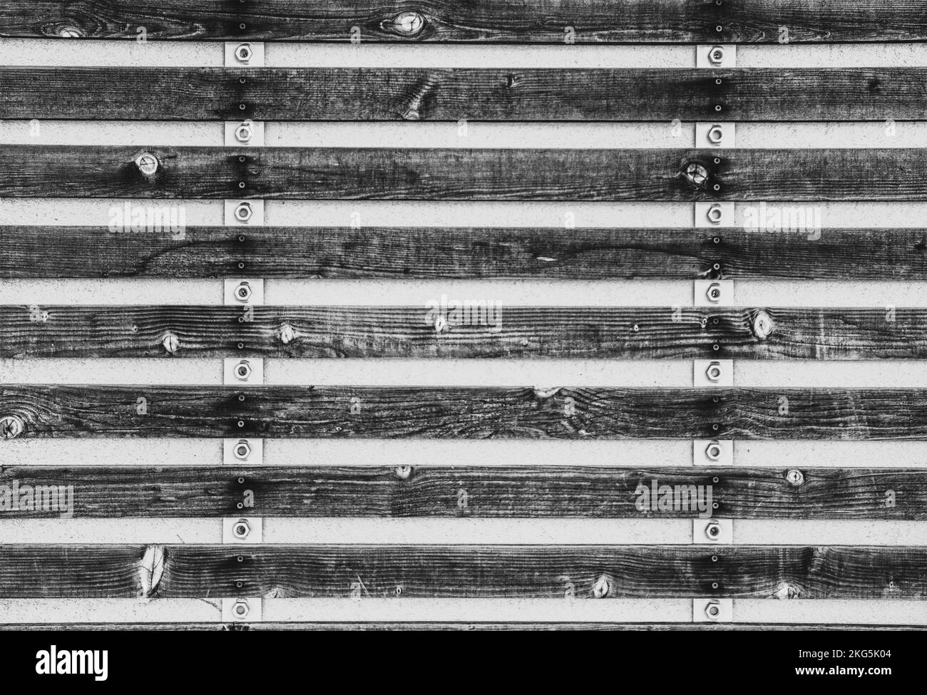Schwarzer und weißer rustikaler industrieller Hintergrund mit Holzplatten, die mit Bolzen an Metallstreifen befestigt sind Stockfoto