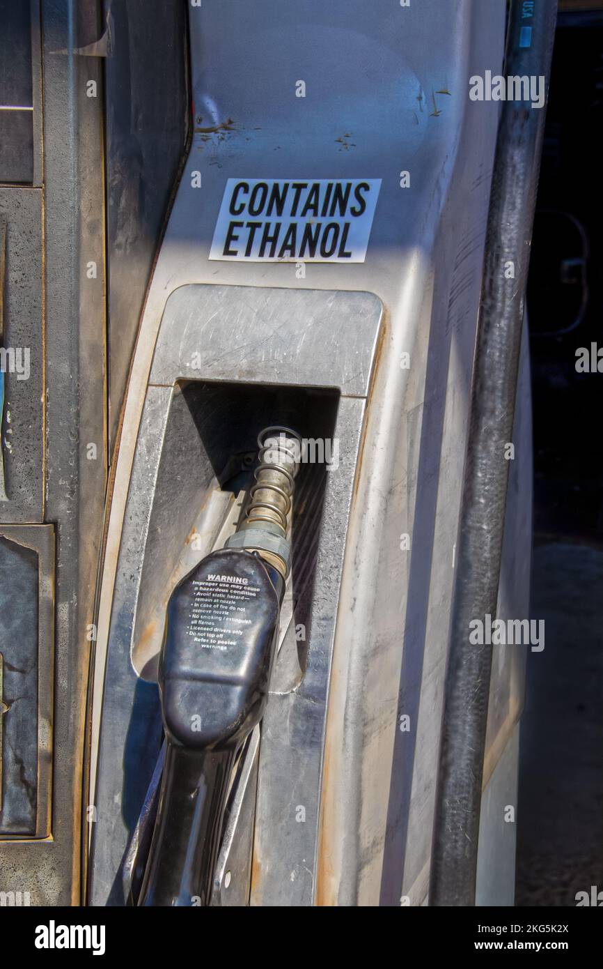Zapfpistole für Benzinkraftstoff in den USA – alt, verbogen und grungelig mit Schild enthält Ethanol und Warnmeldung zum Aufwärmen am Pumpengriff Stockfoto