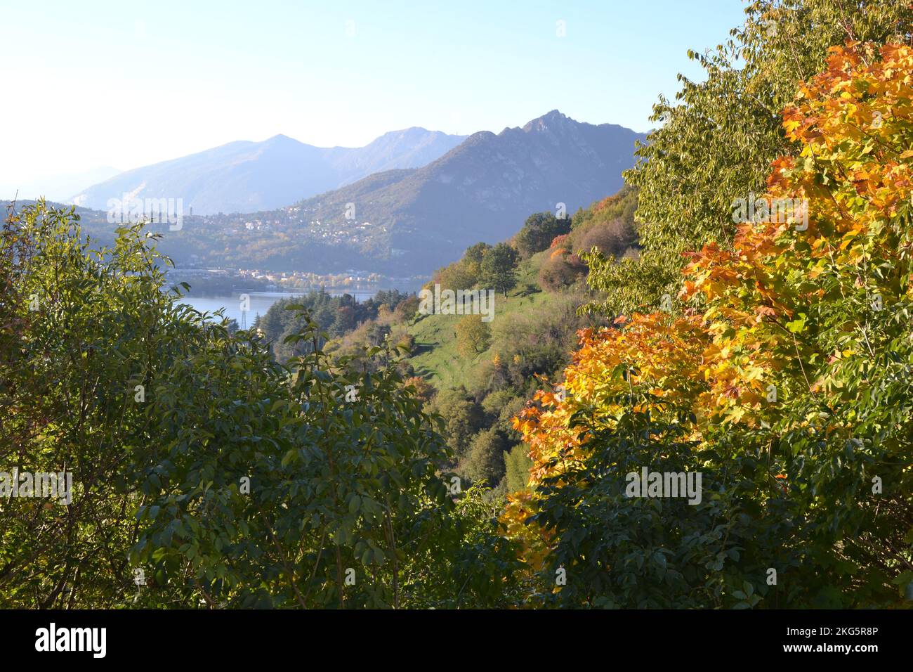 Wunderschöne Herbstlandschaft in Bergen mit Herbstbäumen im Vordergrund. Verwischen Sie die Berge und den See im Hintergrund. Mehrstufiges Panorama. Stockfoto