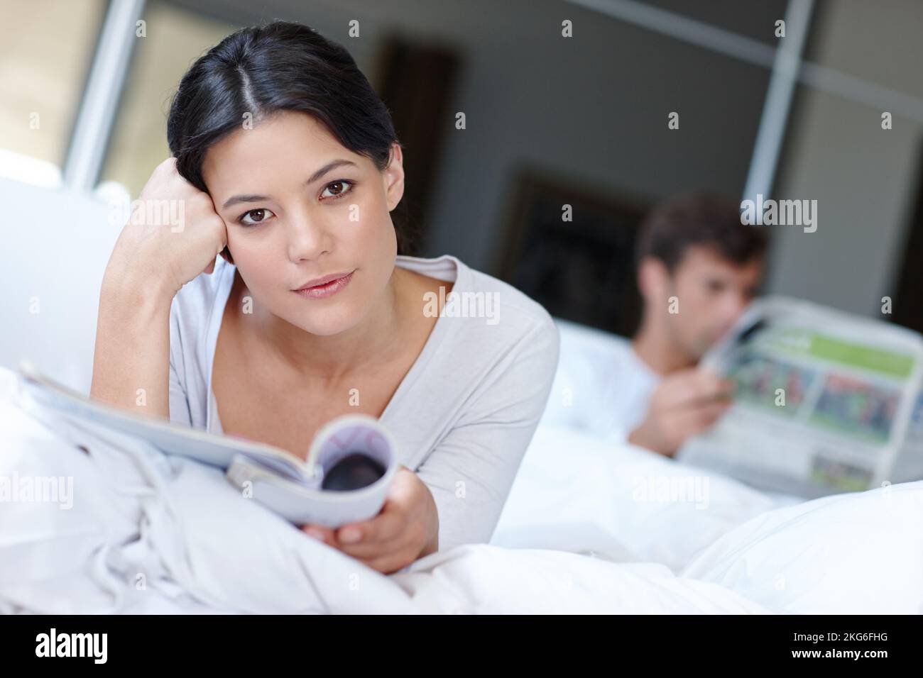Dieser Artikel hat mich zum Nachdenken gebracht. Eine schöne Frau, die im Bett liegt und eine Zeitschrift liest. Stockfoto