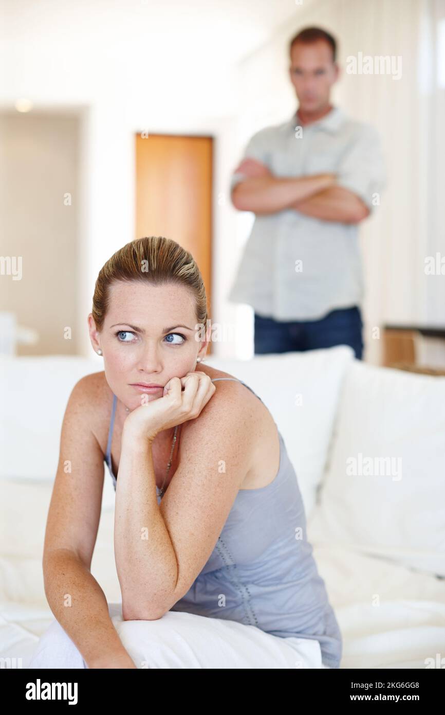 Probleme im Paradies. Eine Frau sitzt und schaut aufgeregt, während ihr Mann im Hintergrund steht. Stockfoto