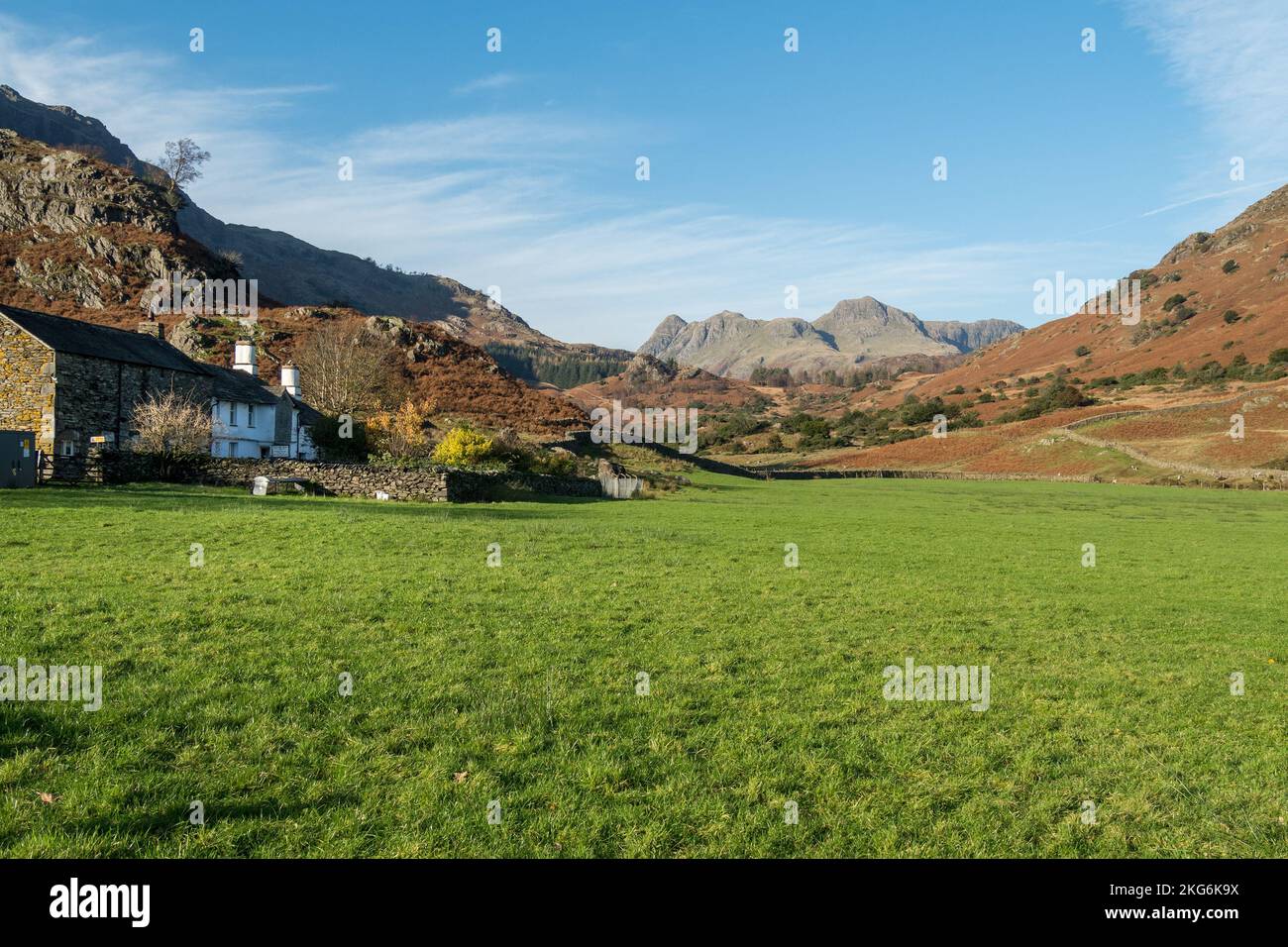 Green Grassy Field und Fell Foot Farm in Little Langdale mit der Langdale Pikes Mountain Range in der Ferne, English Lake District, Cumbria, Großbritannien Stockfoto