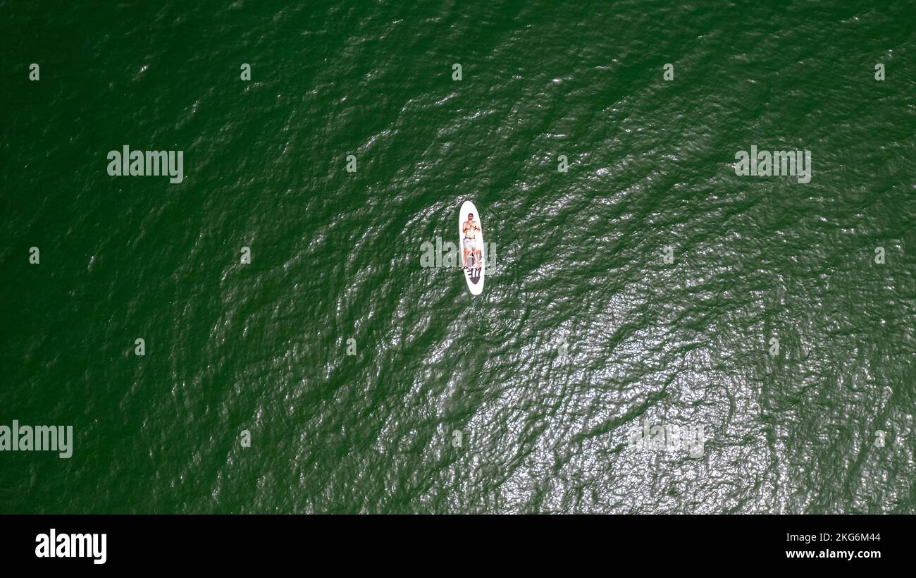 Drohnenaufnahme eines Surfers auf einem Surfbrett mitten im Ozean. Stockfoto
