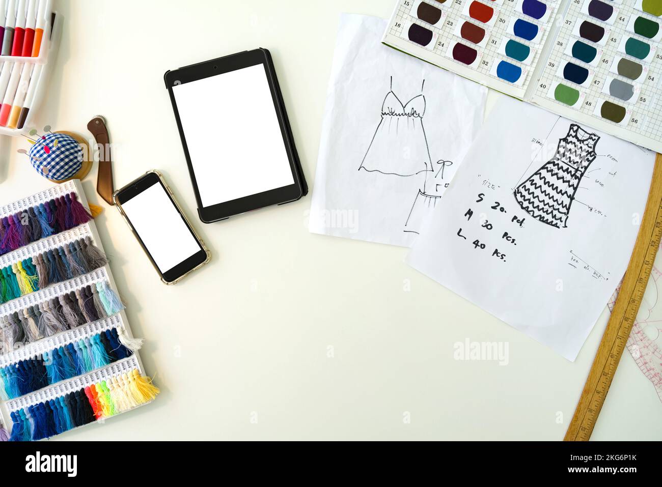 Modedesignerzimmer. Mobiltelefon, Tablet-Computer, Muster für Stoff, Farbmusterkatalog mit Seidenfaden, mehrfarbige Magic Stifte und Skizzen Stockfoto