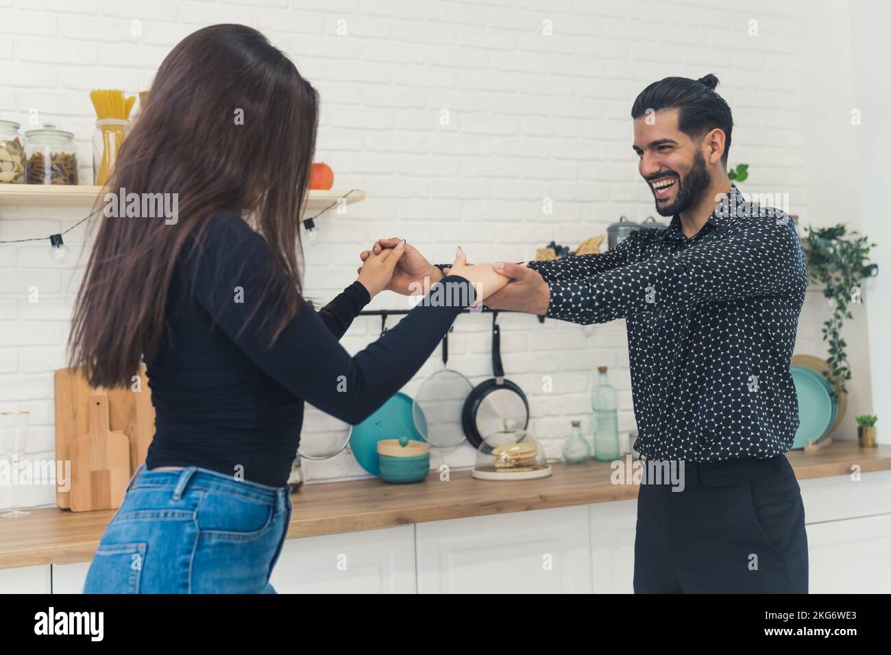Ein junges, fröhliches, elegantes Paar, das lacht, Händchen hält, in der Küche in seiner neuen hellen Wohnung tanzt, den Umzug feiert. Hochwertiges Foto Stockfoto