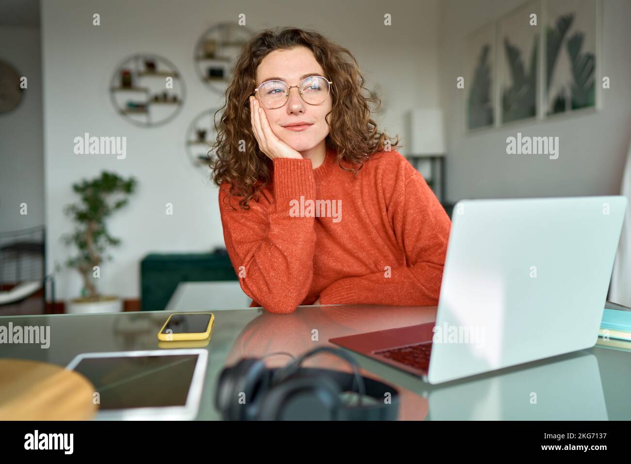 Junge Frau, die zuhause an einem Laptop arbeitet und wegsieht und denkt. Stockfoto