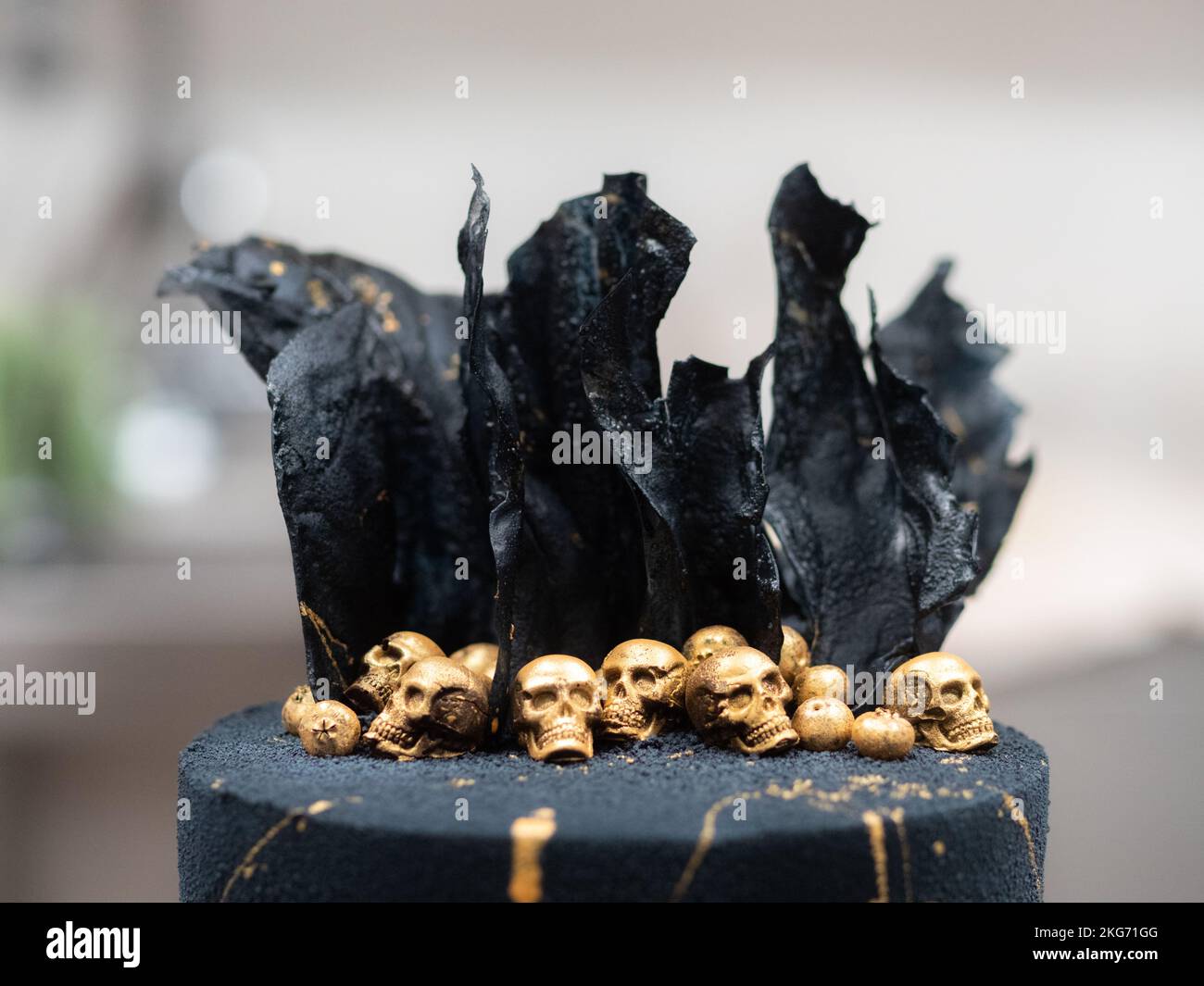 Der Konditormeister schmückt den schwarzen Muertos-Geburtstagskuchen mit goldenen essbaren Schädeln und schwarzen Reispapiersegeln Stockfoto