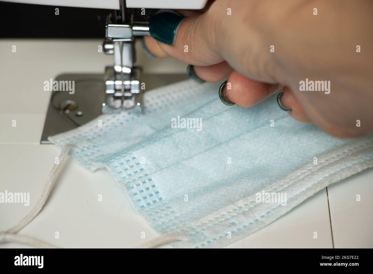 Eine medizinische Maske liegt auf einer Nähmaschine und die Hand einer Frau liegt auf dem Tisch, näht medizinische Masken, Herstellung von medizinischen Masken Stockfoto