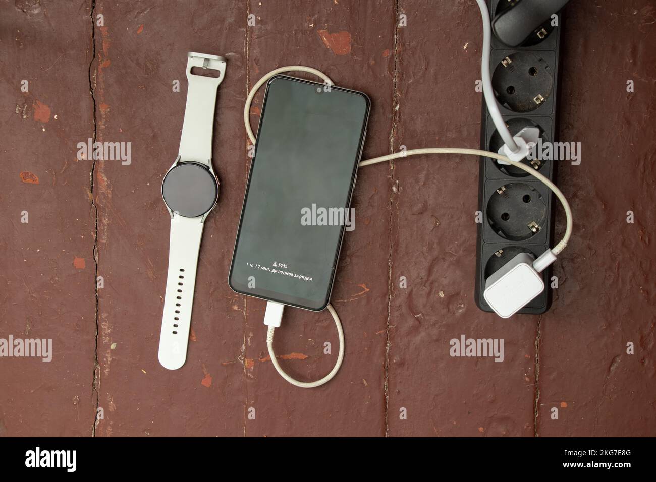 Telefon und Smartwatch werden in der Nähe der Buchse am Tisch aufgeladen, sodass das Telefon aufgeladen wird Stockfoto