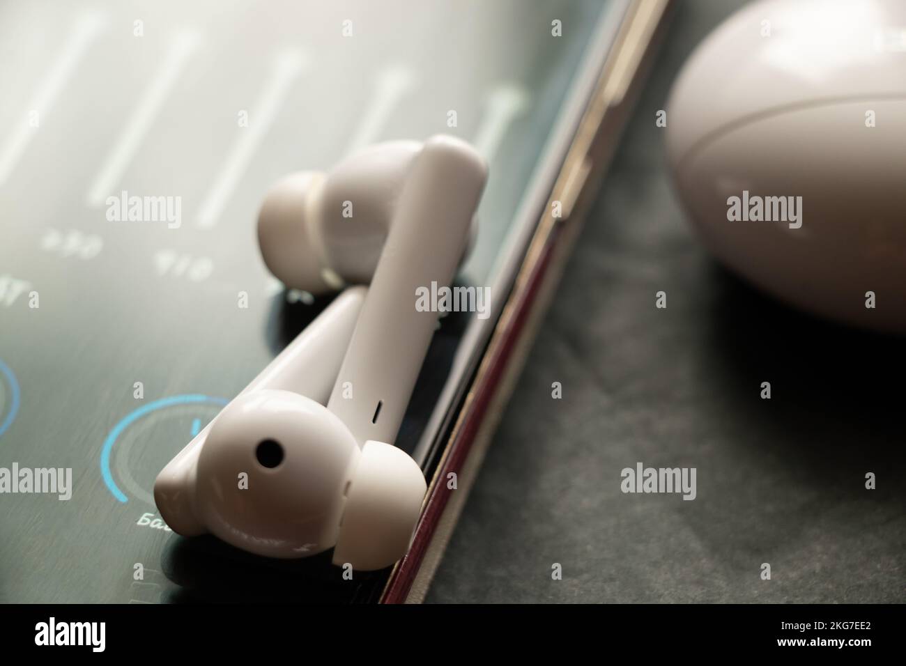 Kabellose weiße Kopfhörer und ein Equalizer im Telefon, Online-Musik im Telefon und Lieder Stockfoto