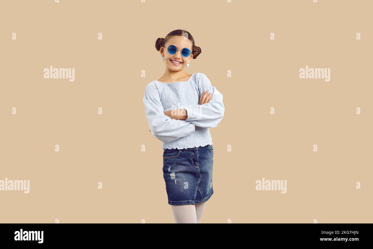 Glückliches hübsches Mädchen in trendigen, lässigen Outfit und Sonnenbrille mit beigefarbenem Hintergrund Stockfoto