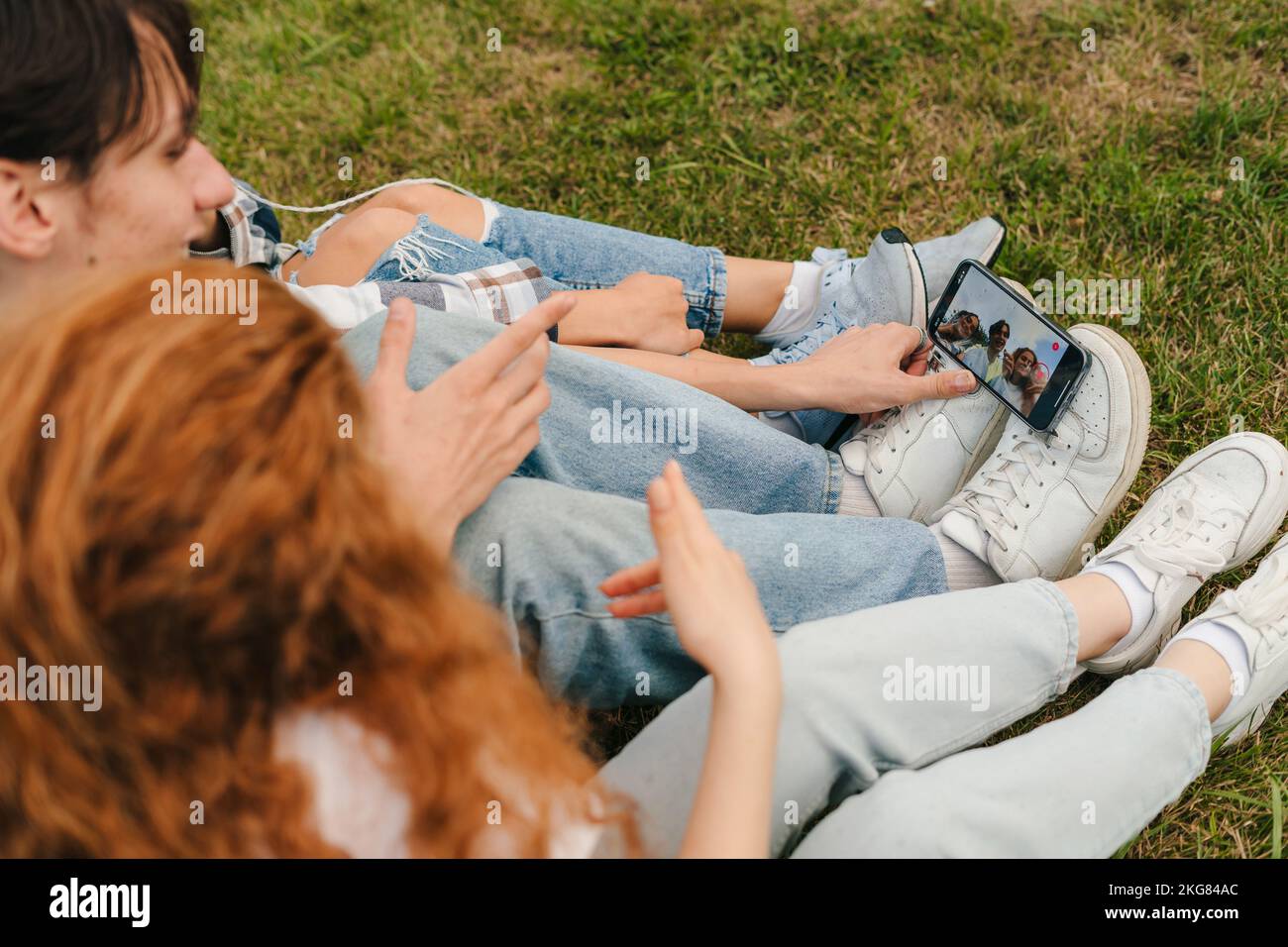 Drei Influencer posieren in sozialen Netzwerken, die im Park nachbilden und auf grünem Gras sitzen. Mobiltelefonkommunikation. Internet Stockfoto