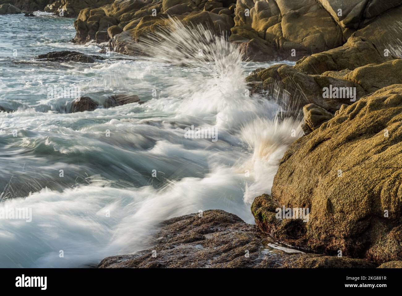 Wellen stürzen auf die Felsen am Chahue Beach auf den Bahias von Huatulco, Mexiko. Eine langsame Verschlusszeit verleiht dem Wasser einen seidigen Look. Stockfoto
