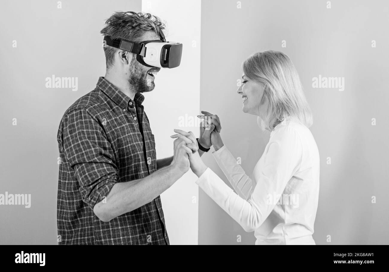 Man VR-Brillen genießen Videospiele. Das beste Geschenk aller Zeiten. Der Mensch genießt die virtuelle Realität. Ein Mädchen, das froh ist, dass es ihr Geschenk mag. Geschenkideen für Männer. Mach ihn glücklich, schenke ihm etwas Stockfoto