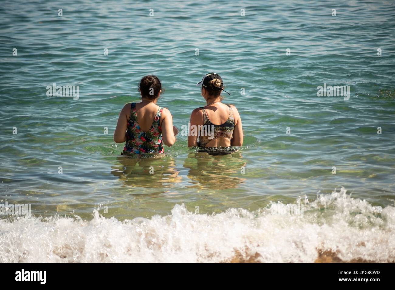 Mutter und Tochter im Bikini beim Wassereintritt am Strand von Porto da Barra in Salvador, Bahia Stockfoto