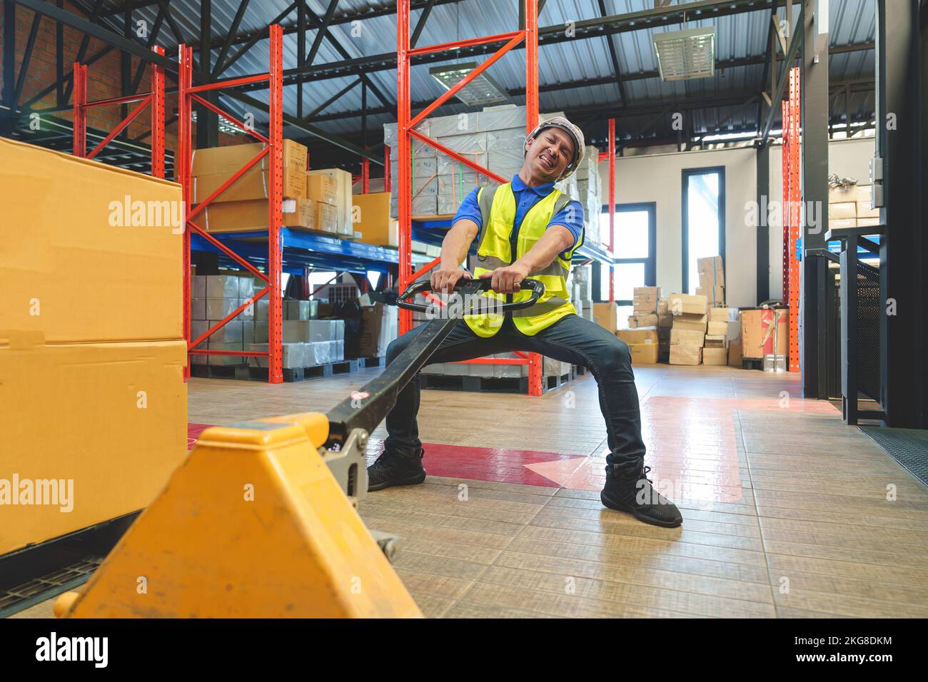 Asiatischer Lagerarbeiter, der einen Palettenhubwagen zieht. Arbeiter, der mit einem manuellen Palettenhubwagen arbeitet, entlädt Frachtkisten auf Paletten im Lager. Stockfoto