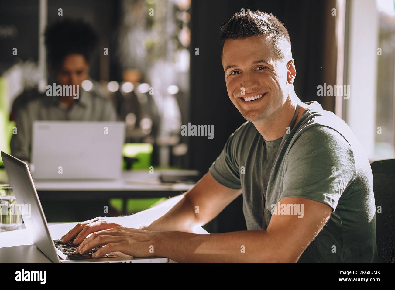 Ein fröhlicher junger Mann, der an seinem Arbeitsplatz für die Kamera posiert Stockfoto