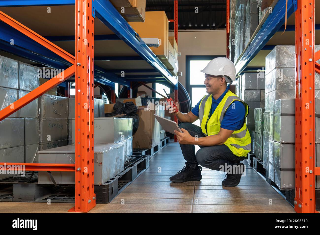 Asiatischer männlicher Dispatcher überprüft Pakete, während er Walkie-Talkie im Vertriebslager benutzt. Stockfoto