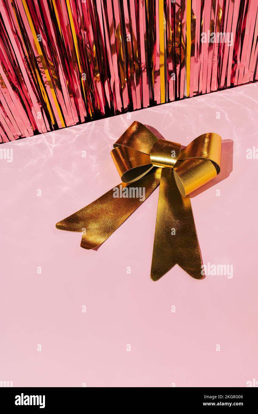 Goldfarbene Schleife auf pinkfarbenem Hintergrund mit glänzenden Weihnachtstinketten. Neujahrsgrüßungskonzept. Stockfoto