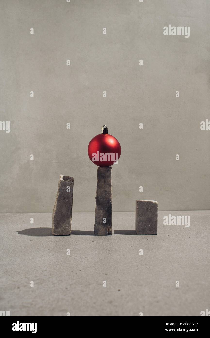 Rote Weihnachtskugel, die auf einem natürlichen grauen Stein steht. Minimales Begrüßungskonzept. Stockfoto