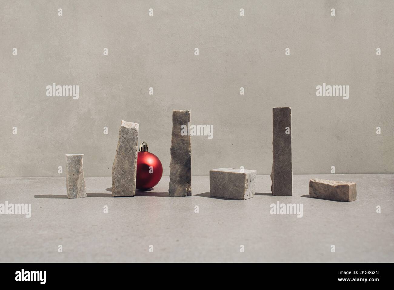 Rote Weihnachtskugel zwischen senkrechten Teilen aus Naturstein. Minimales Begrüßungskonzept. Stockfoto
