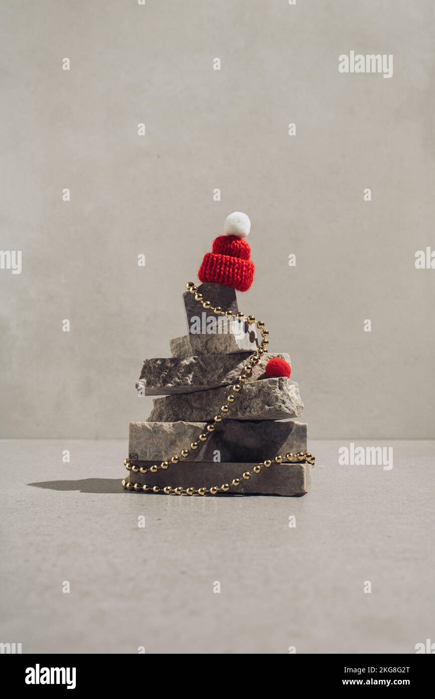 Roter Winterhut auf einem Weihnachtsbaum aus Naturstein mit Goldperlen. Minimales Begrüßungskonzept. Stockfoto