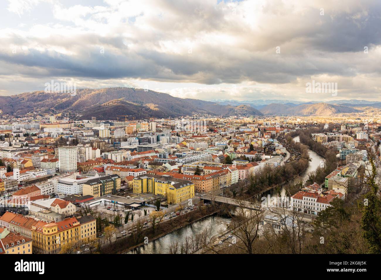 Stadtbild von Graz, Fluss Mur und umliegende Berge. Bunte Wolken und Sonnenschein, Wintertag. Graz, Steiermark, Österreich. Stockfoto