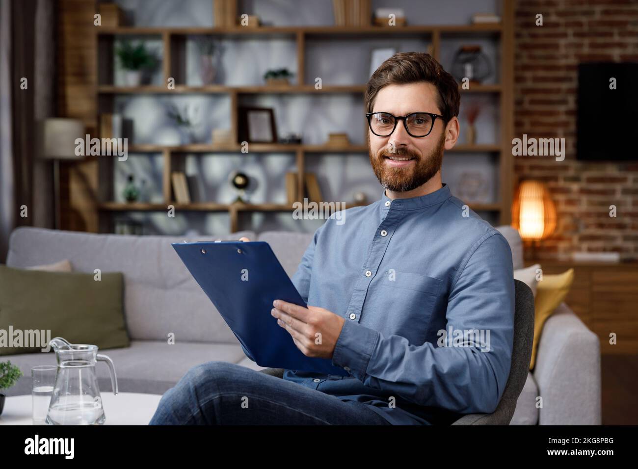 Ein gutaussehender Erwachsener sitzt zu Hause in einem stilvollen Büro. Psychologe, Trainer oder Geschäftsmann, der in die Kamera schaut und lächelt. Schöne Zähne und Stockfoto