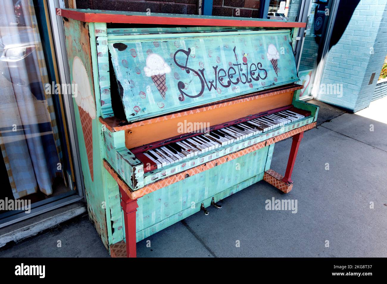 Auf dem Bürgersteig wurde ein zerbrochenes Klavier mit Werbung für den Sweeties Ice Cream Shop in der Nähe dekoriert. Fergus Falls, Minnesota, USA Stockfoto