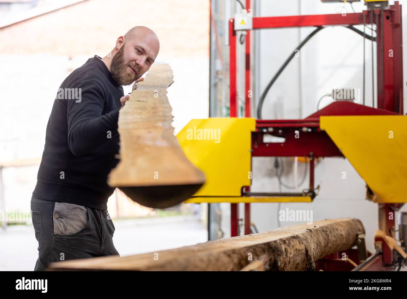 Junger Mann, der an der Maschine für die Holzverarbeitung arbeitet, großer Holzschneider oder Säge, Industriekonzept Stockfoto