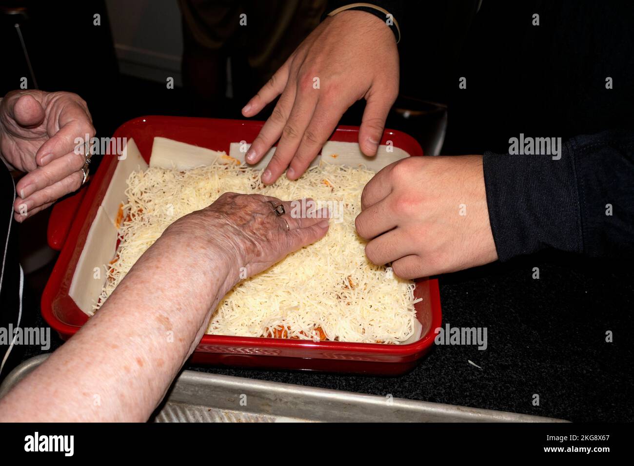 Hände von Großmutter und Enkel, die zu Hause eine vegetarische Lasagne machen. St. Paul Minnesota, USA Stockfoto