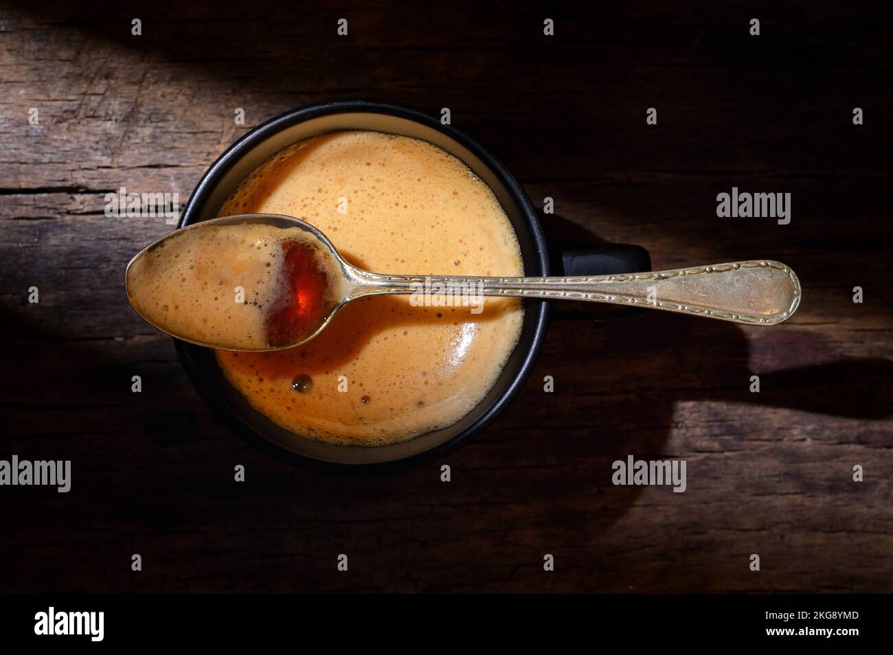 Schwarzer Espresso-Becher und Löffel mit Schaumstoff auf Holztisch Stockfoto