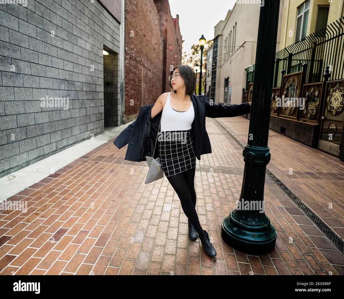 Joyful Young Woman schaukelt auf einem Lampenpfahl | Business Freizeitkleidung Stockfoto