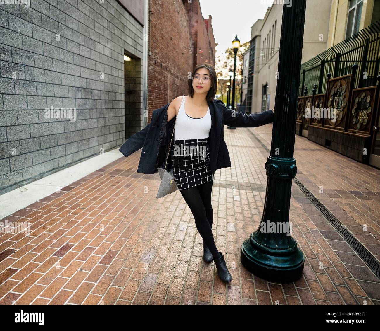 Joyful Young Woman schaukelt auf einem Lampenpfahl | Business Freizeitkleidung Stockfoto