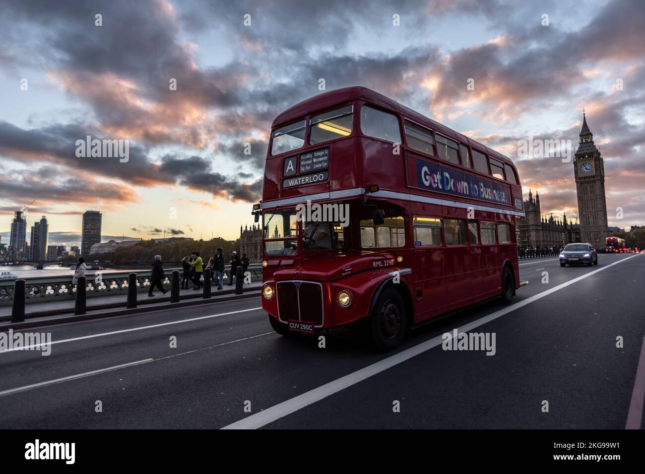 Ein Routemaster-Bus fährt an einem Winterabend entlang der Westminster Bridge, während die Sonnenuntergänge im Westen mit dem Palace of Westminster in der Ferne Großbritannien. Stockfoto