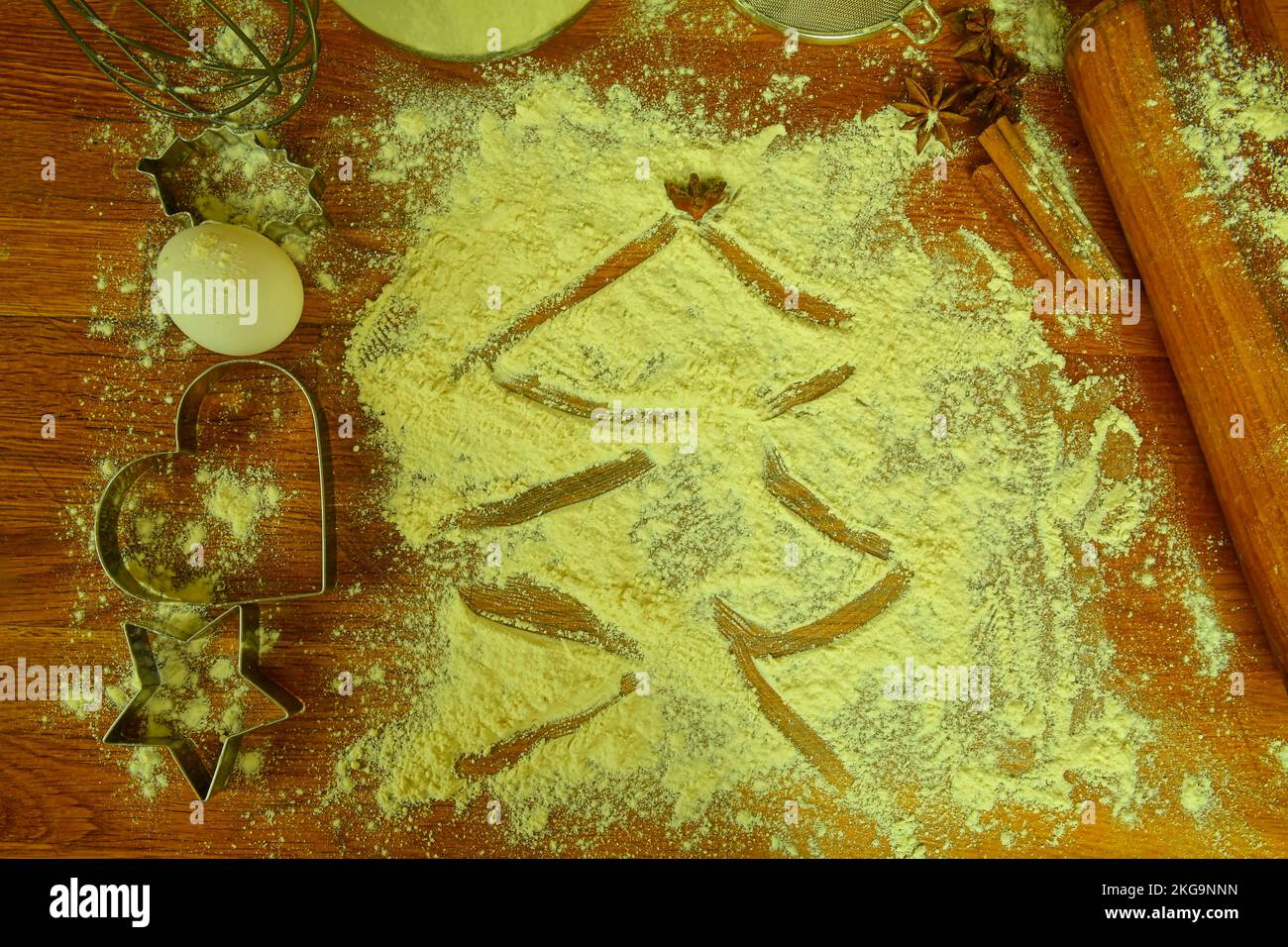 Zutaten zum Kochen von Weihnachtsgebäck: Tannenbaum aus Mehl auf einem braunen Tisch. Küchenutensilien auf dunklem Hintergrund, Blick von oben Stockfoto