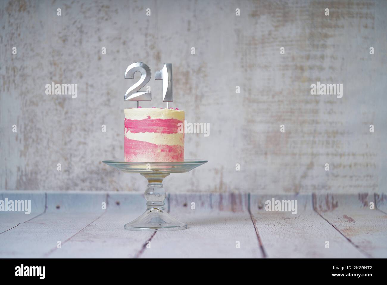 21. Geburtstagskuchen, rosa und silberne Torte mit ein paar Streuseln und 21. Kerzenlicht auf weißem Holzhintergrund. Stockfoto