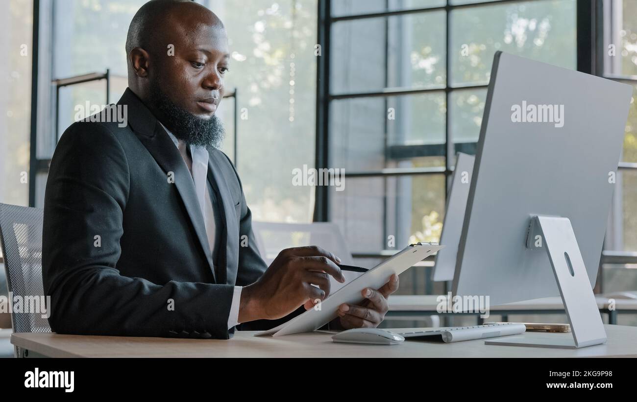 Afrikanischer Autor, der Notizen auf einem Tablet auf Papier schreibt, sitzt am Schreibtisch Erwachsener Unternehmer, amerikanischer Geschäftsmann kreiert neue Ideen Unternehmen Aufgaben Geschäft Stockfoto